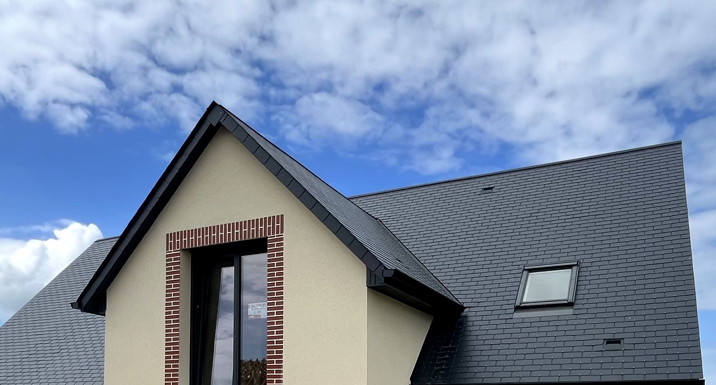 Pignon d'une maison réalisée par FBC : enduit ton pierre, encadrement en brique et couverture ardoise